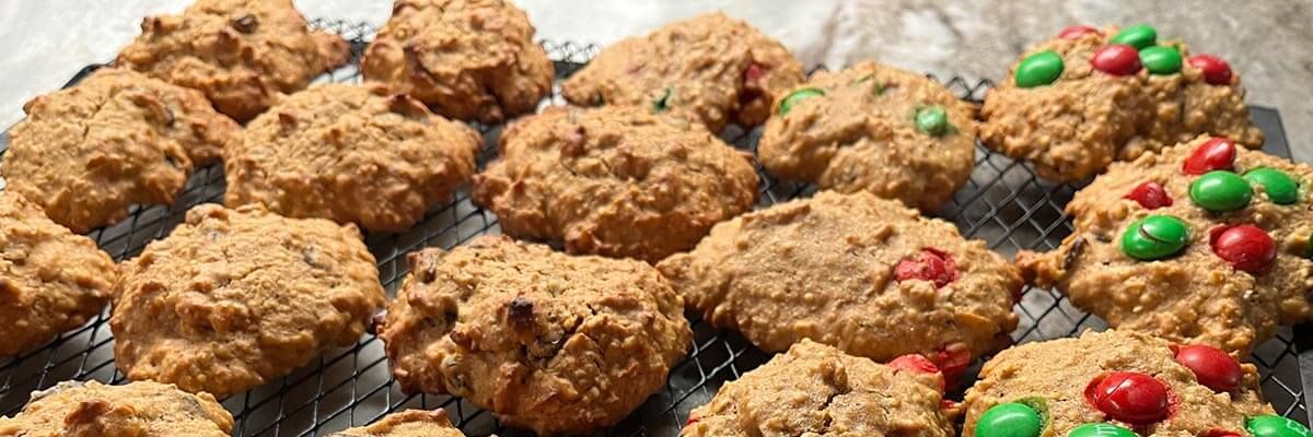 Dense, hearty cookies are displayed on a baking sheet. Four cookies on the right side feature red and green candies.